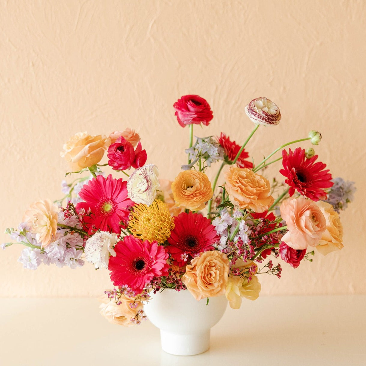 a cheery arrangement of gerbera daisies, ranunculus, pin cushion protea, waxflower and more