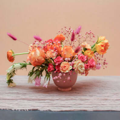 Seasonal flowers in medium low arrangement with pink vase