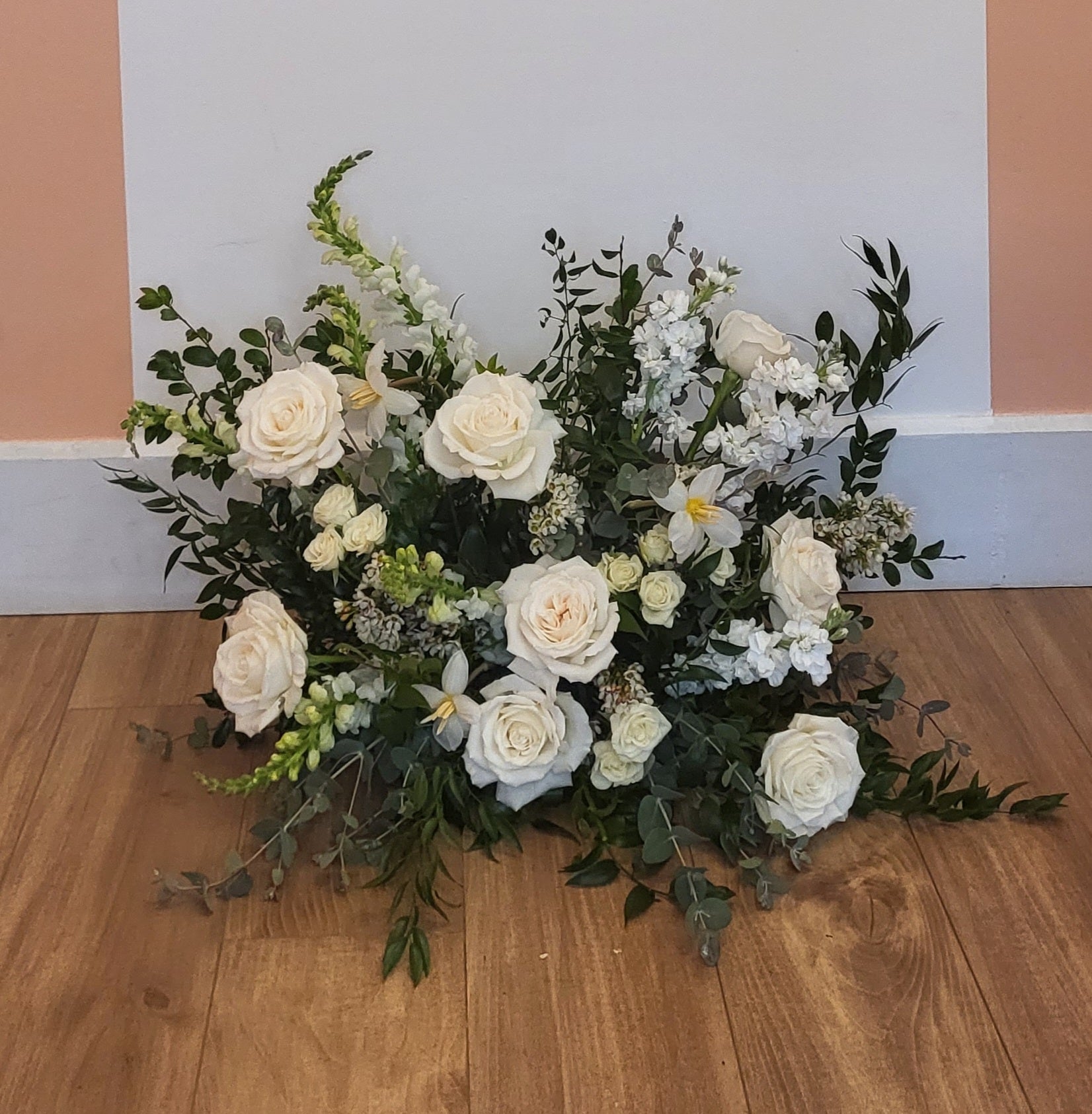 A statement piece of bright white roses, tulips and snapdragons is paired with deep greens and can be used for both the ceremony and reception