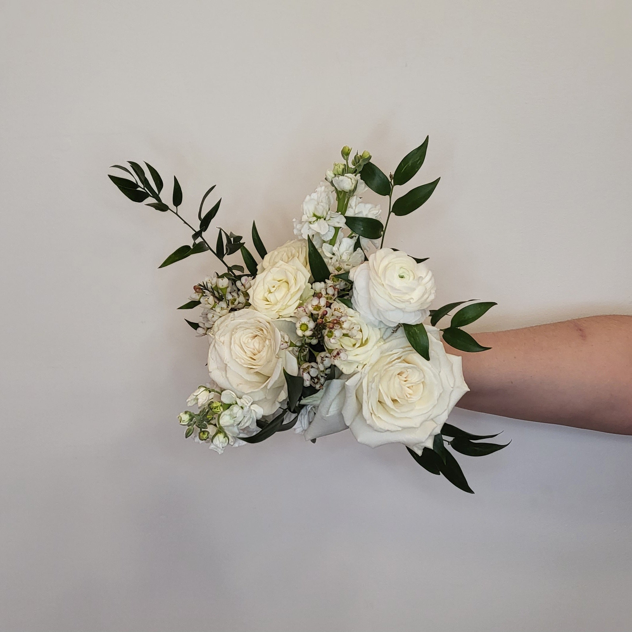 a petite arrangement of white roses, stock, and waxflower with fresh greens