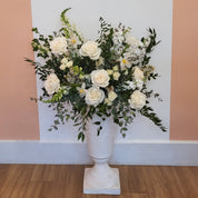 A white urn is overflowing with healthy white flowers and fresh greenery