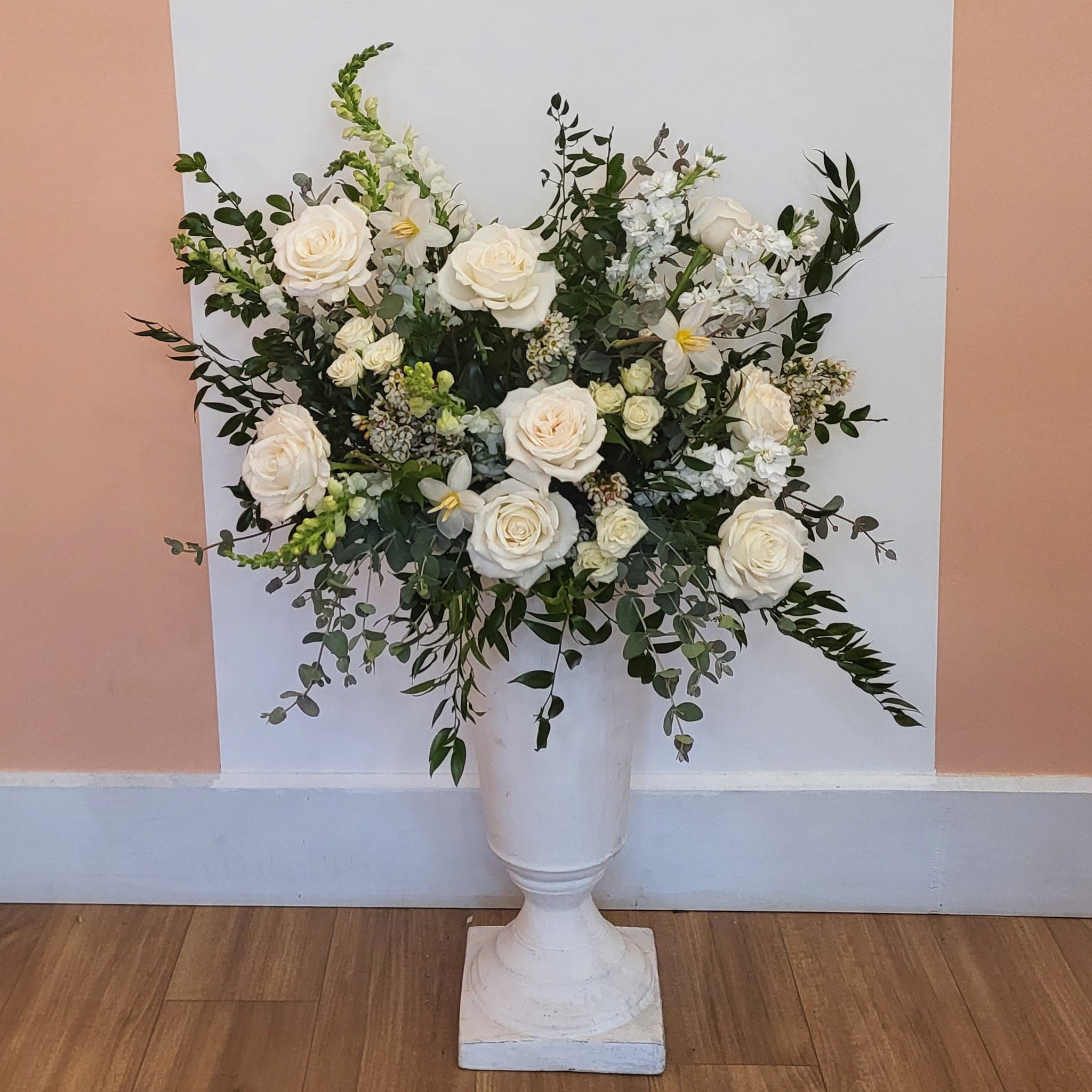 A white urn is overflowing with healthy white flowers and fresh greenery