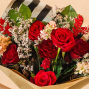 Bouquet of red and green flowers held by a hand against a beige background