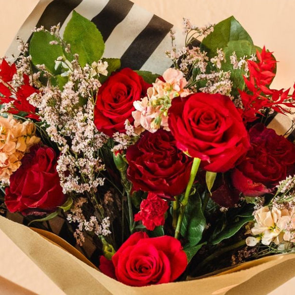 Bouquet of red and green flowers held by a hand against a beige background