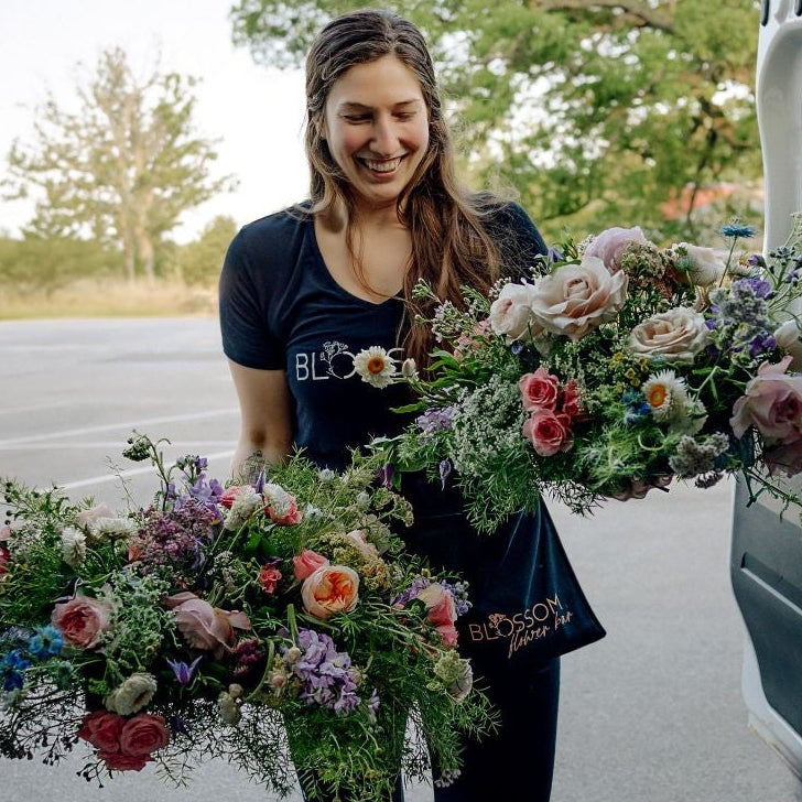 Two large flower arrangements are moved by a smiling Blossom Flower Bar team member