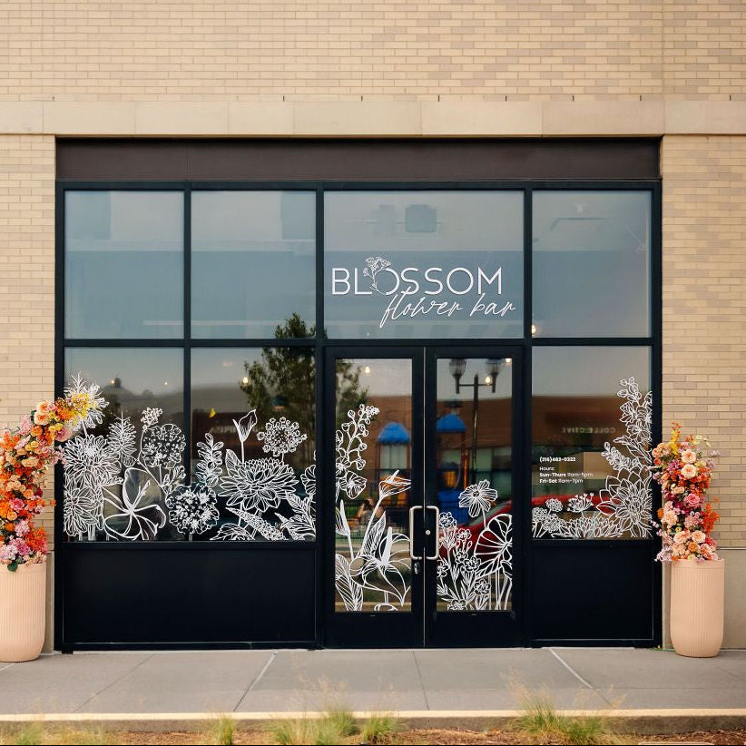 Brick storefront with inviting flower decals in the window and double door with "blossom flower bar" above the doors
