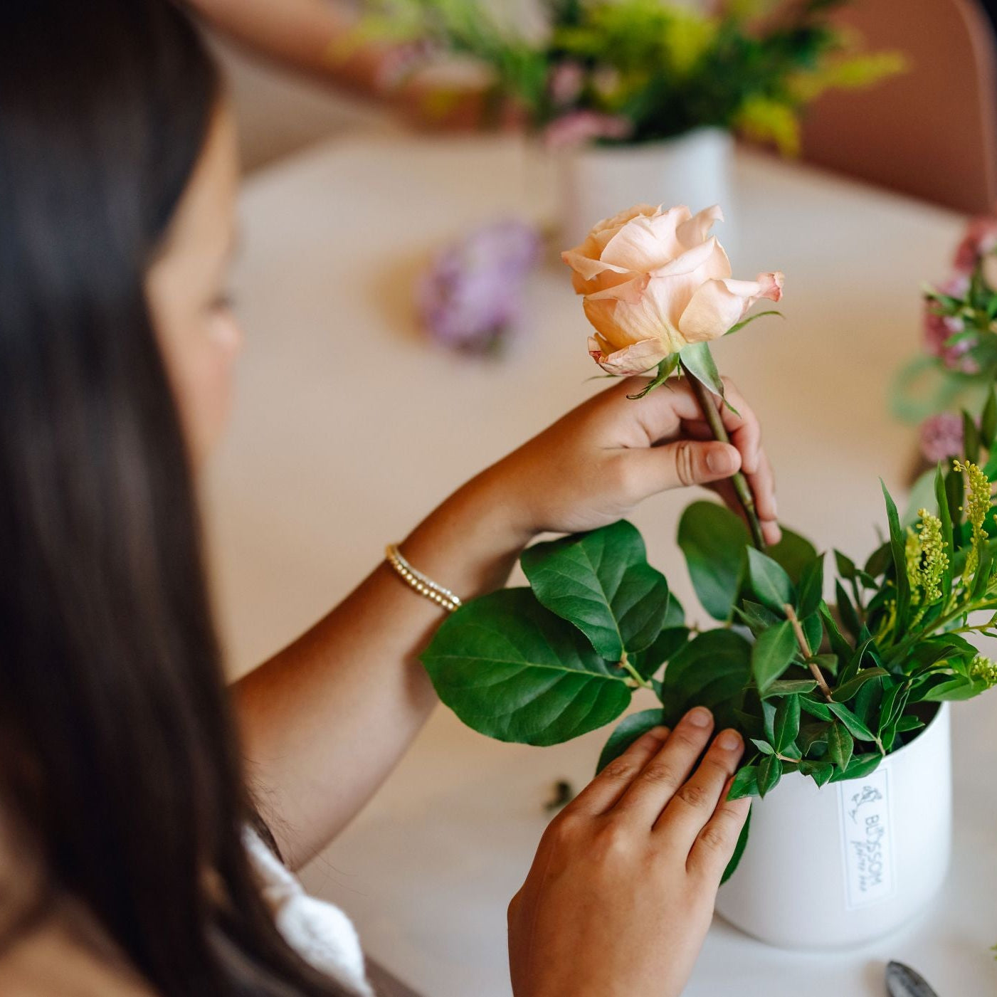 A woman places a rose in an arrangement during a flower design workshop