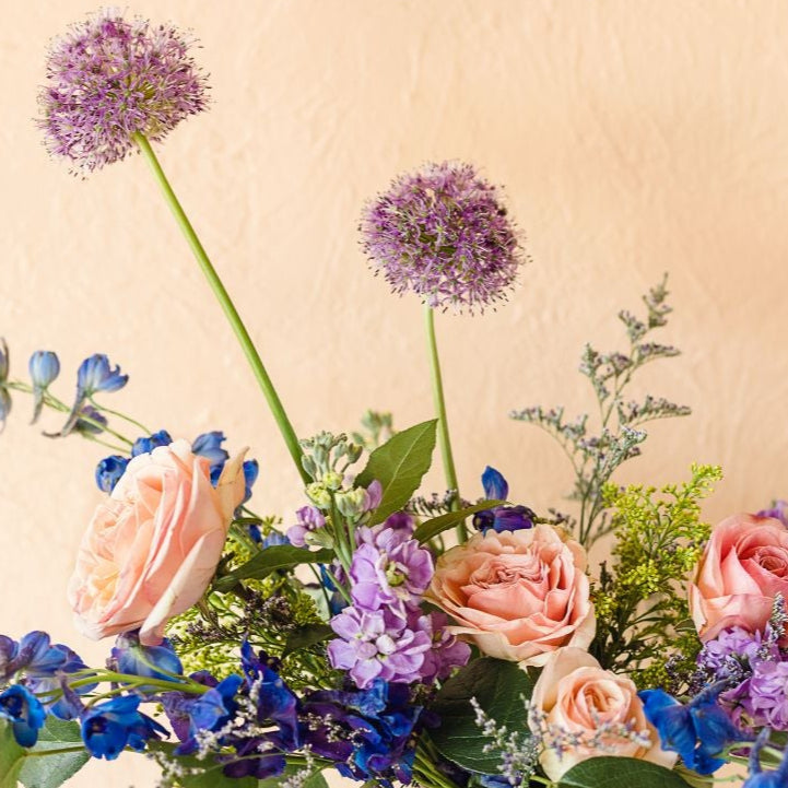 a closeup of healthy and vibrant roses, delphinium, allium and more