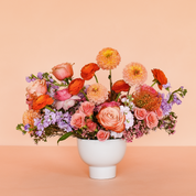 Assorted lush flowers in a low white vase with no filler or greenery