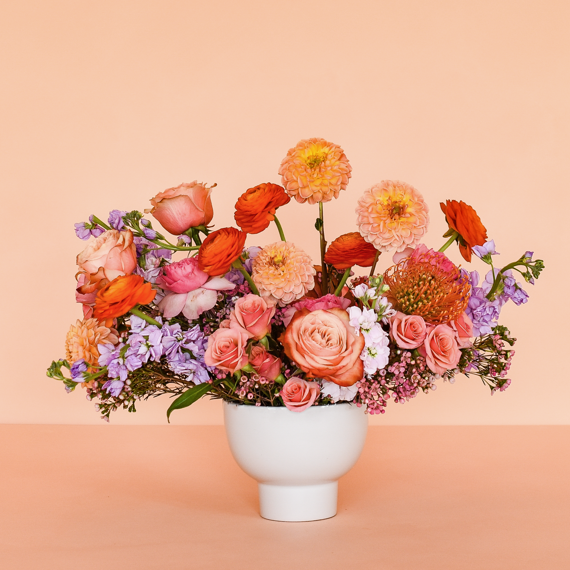 Assorted lush flowers in a low white vase with no filler or greenery