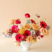 a cheery arrangement of gerbera daisies, ranunculus, pin cushion protea, waxflower and more
