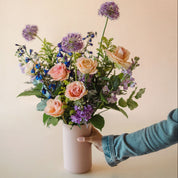 Pale peach roses, bright purple allium, vibrant blue delphinium and more arranged in a vase