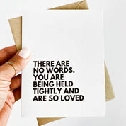 A sympathy card with black text on a white card that reads "there are no words. you are being held tightly and are so loved"