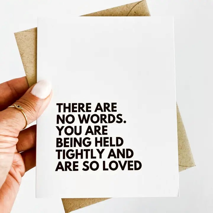 A sympathy card with black text on a white card that reads "there are no words. you are being held tightly and are so loved"