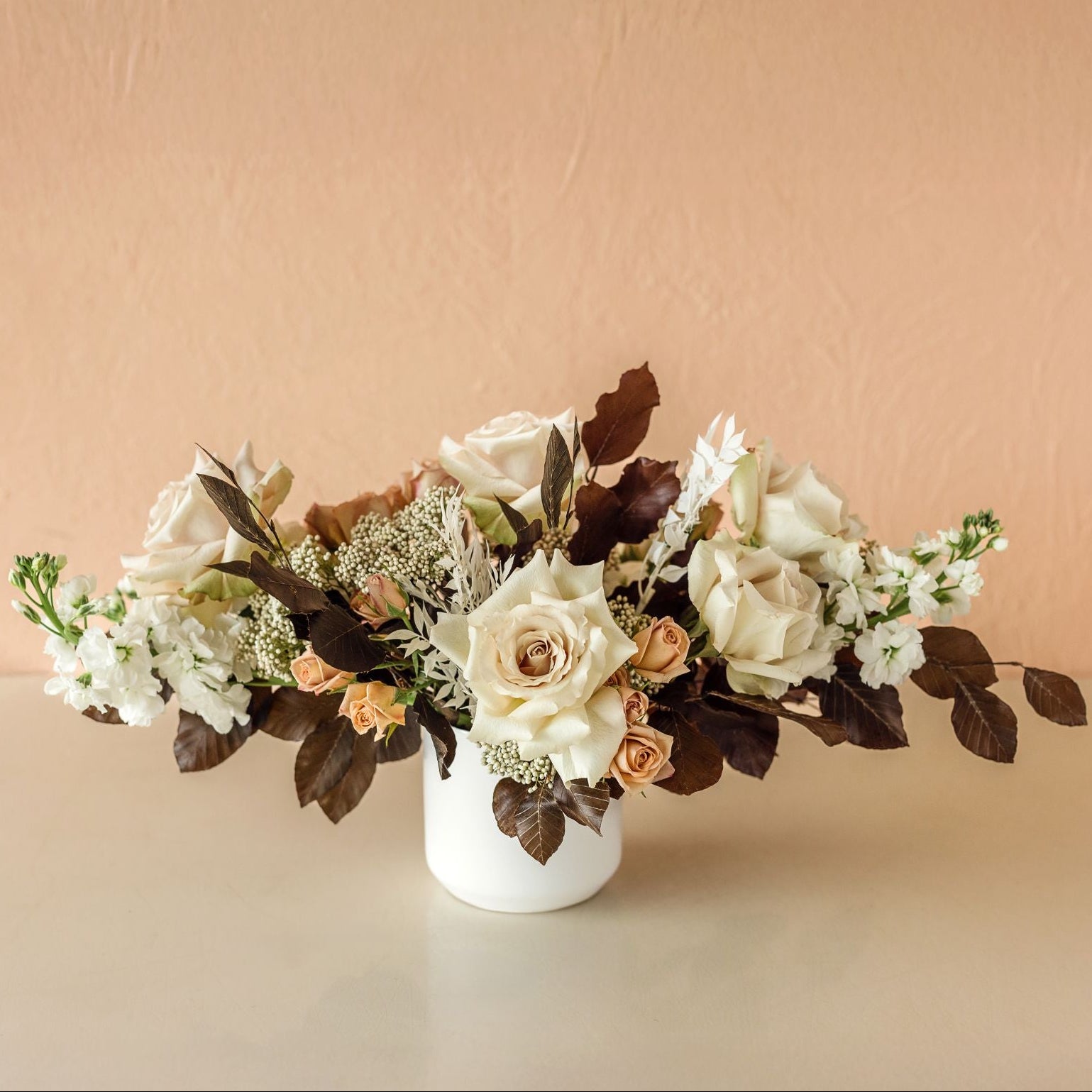 A vased arrangement with white, cream and tan flowers and brown accent leaves