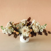 A vased arrangement with white, cream and tan flowers and brown accent leaves
