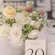 a vased arrangement with peach ranunculus, pink tulips, white spray roses complements a table number and candles
