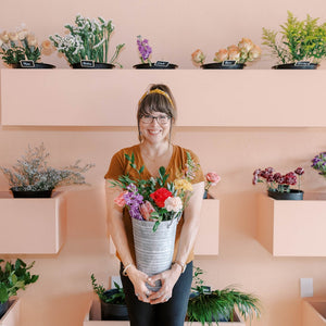 
            
                Load image into Gallery viewer, happy customer standing in front of a wall of flowers
            
        