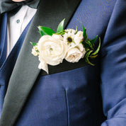 fresh white flowers with greenery peak out of the breast pocket of a dress jacket