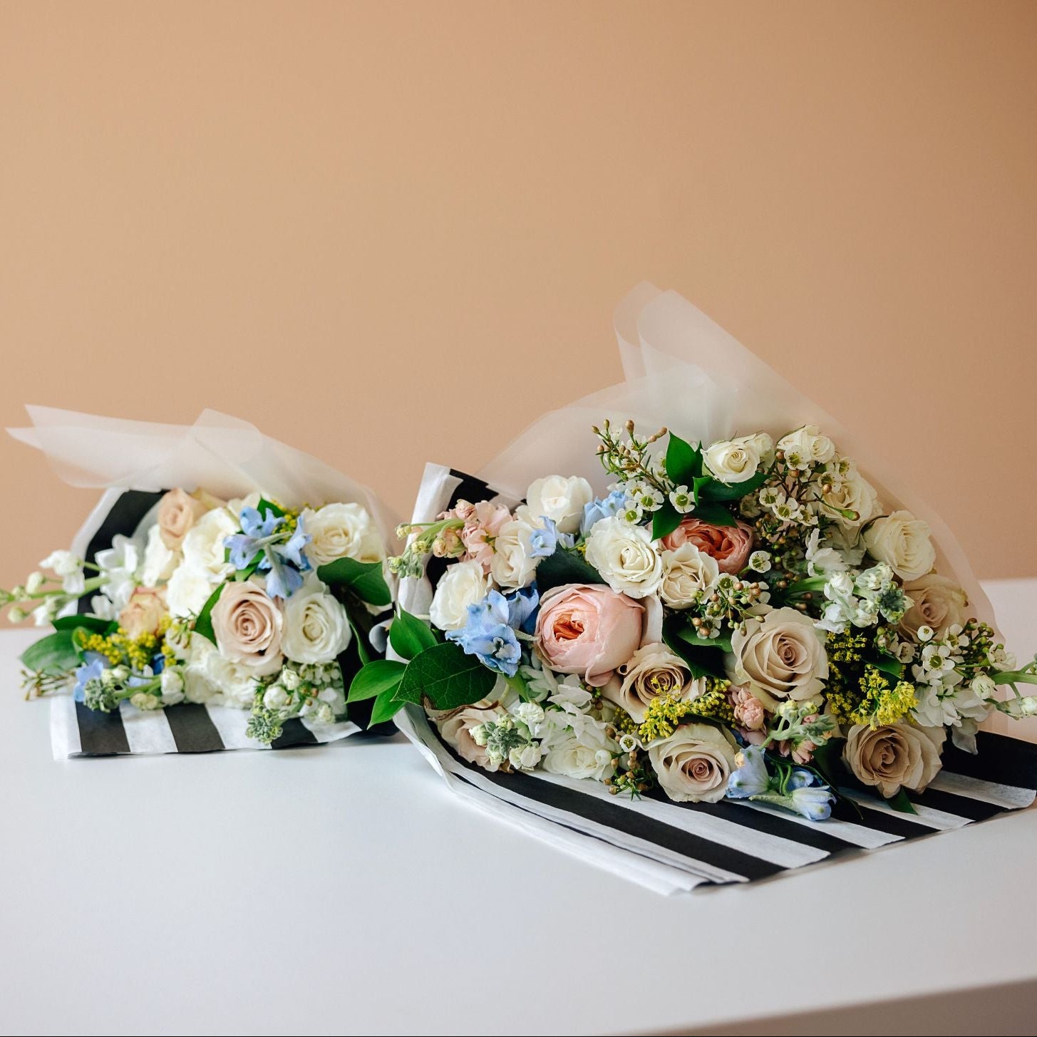 Two floral bouquets with white, blush, and light blue flowers arranged on black-and-white striped paper
