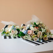 Two floral bouquets with white, blush, and light blue flowers arranged on black-and-white striped paper