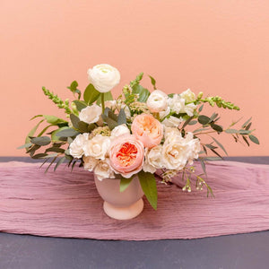 Medium centerpiece with white and pink flowers and greens is a pink vase.